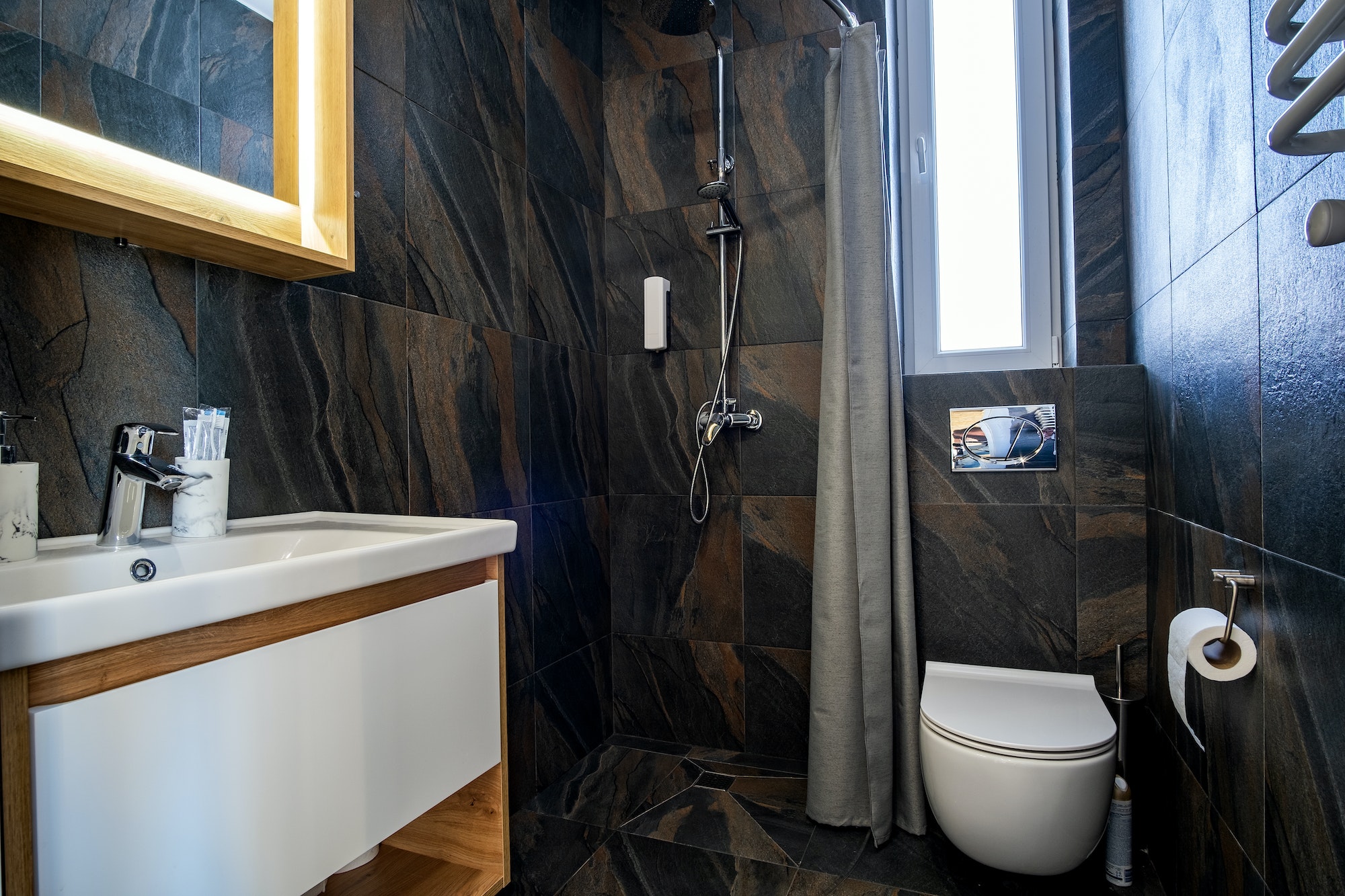 Interior of modern stylish bathroom with black tiled walls, curtain shower place